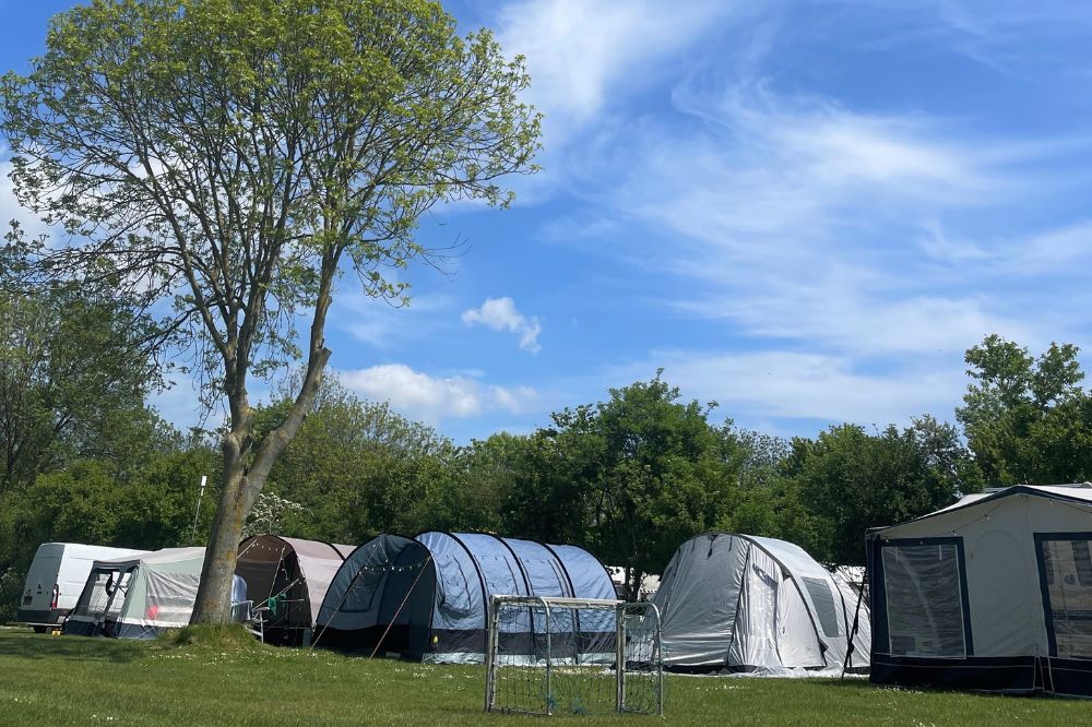 Tenten die gezellig naast elkaar staan  op comfortplaats en een voetbalgoal voor de kids. In de natuur met mooie bomen en bossen en lampjes. 