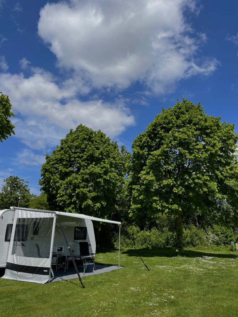 Een caravan op 1 van onze 100 comfortplaatsen in de natuur, tussen de bomen met een bijzettent. Op een prachtig groen grasveld. Mooie comfortplaats in Franeker